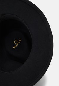 Sombrero de fieltro negro con ala ancha, que presenta una textura suave y un logo dorado que dice "BRIXTON" en el interior de la copa.