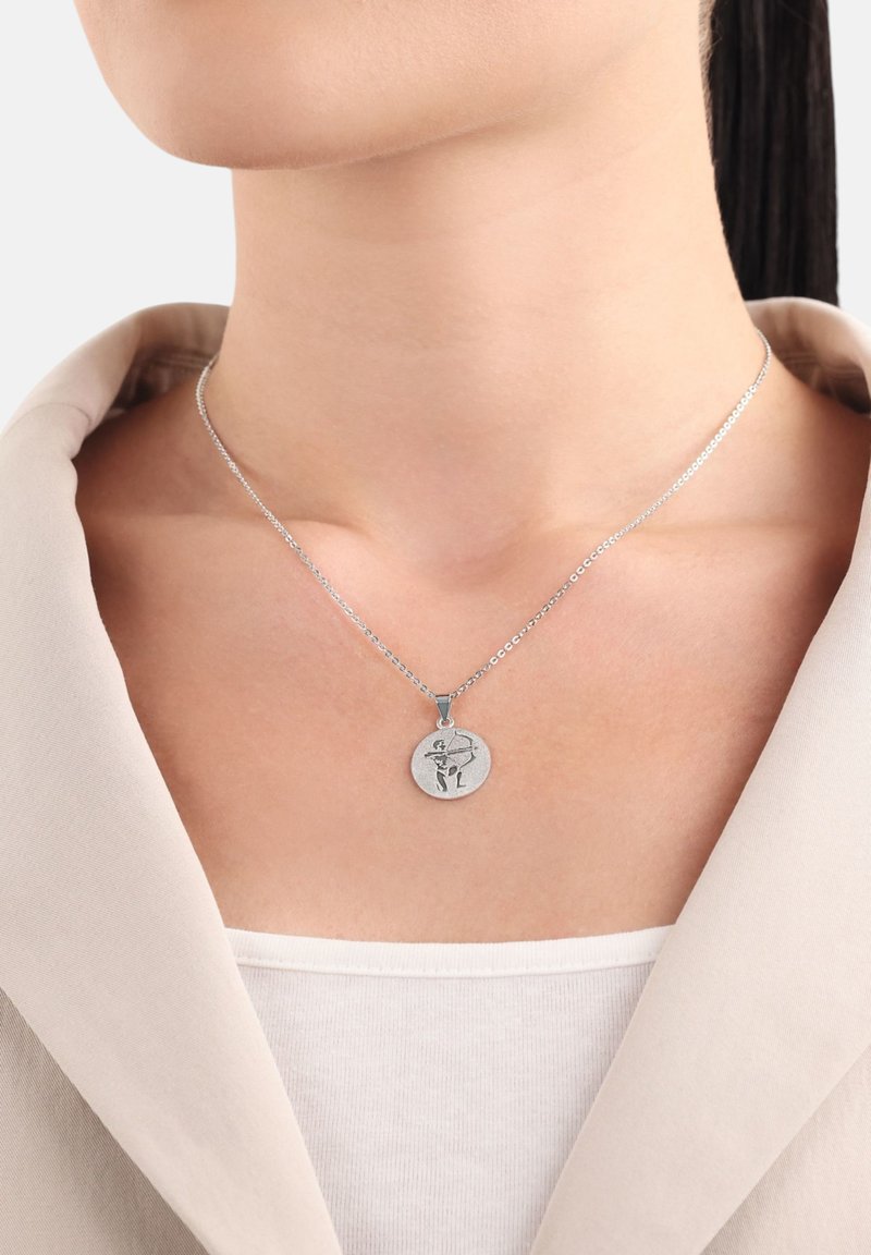 Silverkedjehalsband med ett runt hänge som har en ingraverad design. Hängsmycket är texturerat och hänger framträdande mot en neutral topp.