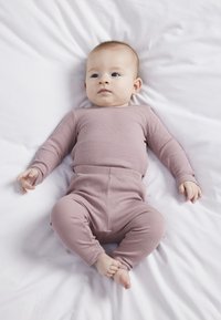 Różowa, prążkowana bluzka z długim rękawem i pasujące spodnie na niemowlęciu, ułożone na białej tkaninie. Rękawy i spodnie mają dopasowane mankiety.
