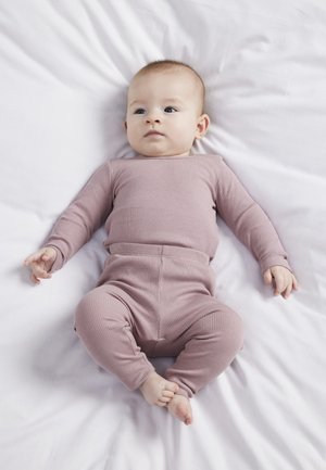 Roze geribbelde longsleeve top en bijpassende broek op een baby, gelegd op een witte stoffen ondergrond. Mouwen en broek hebben aansluitende manchetten.