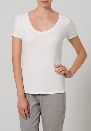 White cotton t-shirt with a scoop neckline and short sleeves. Soft texture with a relaxed fit, paired with gray pajama bottoms.
