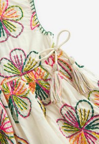 Ärmeloses, besticktes Kleid aus leichtem Stoff mit bunten Blumenmustern in Pink, Gelb und Grün. Bänder mit dekorativen Quasten.