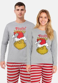 Giovane uomo e donna in pigiami grigi con il testo "Feelin' Grinchy", un'immagine del Grinch, e pantaloni a righe rosso e grigio, sorridenti.