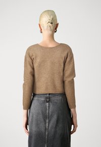 Καφέ πλεκτό πουλόβερ με κοντή εφαρμογή, στρογγυλή λαιμόκοψη και μακριά μανίκια, συνδυασμένο με φούστα από γκρίζο τζιν ψηλής μέσης.