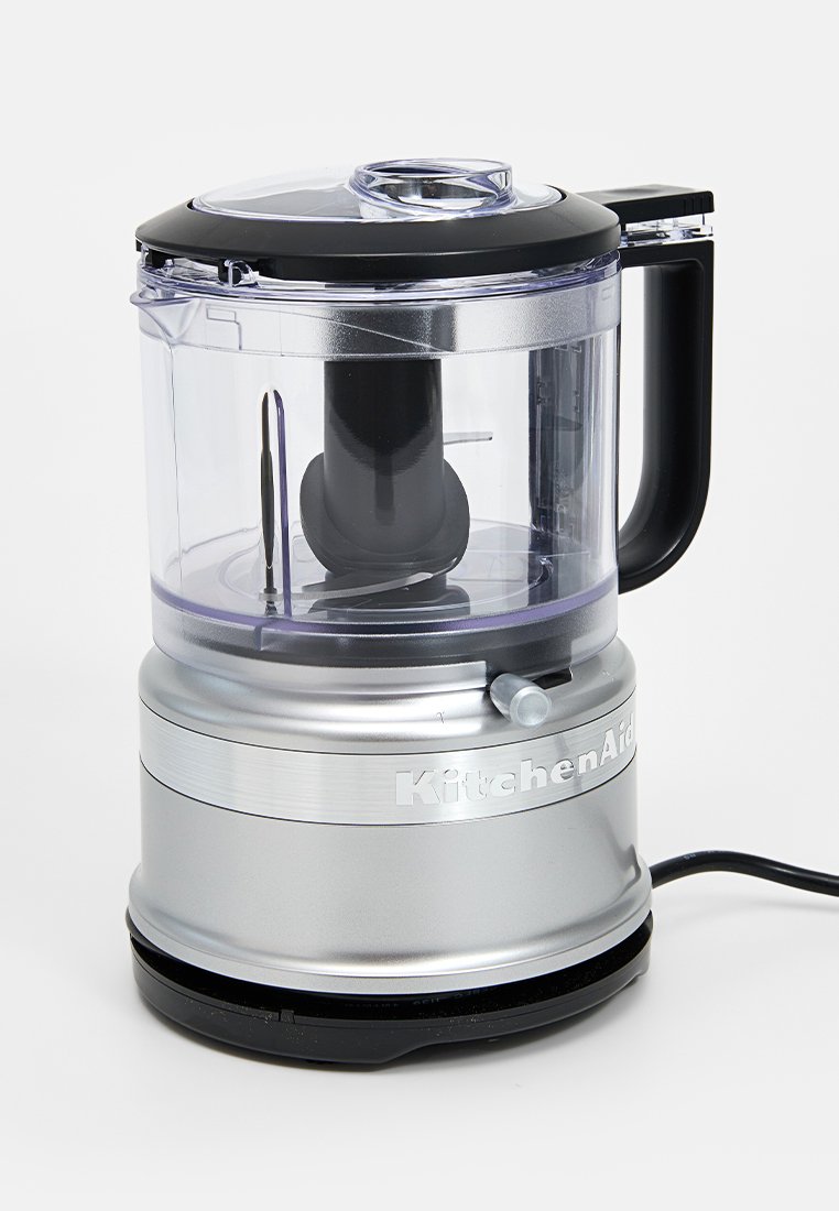 Robot da cucina KitchenAid con ciotola in plastica trasparente, coperchio nero e base argentata. Presenta una maniglia singola e un cavo di alimentazione.