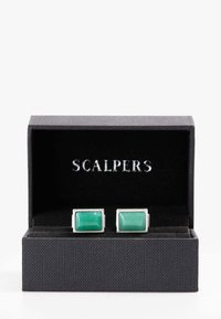 Gemelos de piedra verde enmarcados en un marco rectangular de tono plateado, presentados en una caja negra texturizada con un interior de terciopelo.