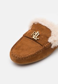 Chausson mocassin en daim marron avec doublure en fourrure beige et logo RL doré sur le dessus, présenté sur un fond blanc.
