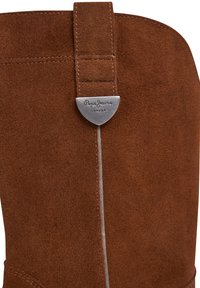 Brūni zamša zābaki ar izšūtu cilpiņu un sudraba krāsas metāla birku ar ierakstu "Pepe Jeans London" uz kājas daļas.