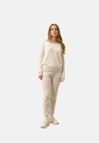 Pull beige lavorato a maglia con polsini a coste abbinato a pantaloni della tuta beige. Modello che indossa sneakers di tonalità chiara. Design semplice con tessuto testurizzato.