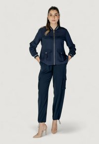 Tuta da uomo navy con giacca con zip, due tasche frontali e polsini elasticizzati. I pantaloni presentano tasche cargo e orli regolabili.