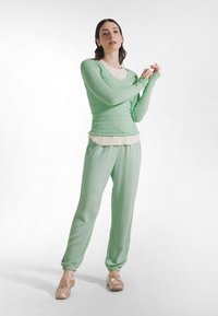 Top de manga larga color verde claro con textura, superpuesto sobre una camisa color crema, combinado con pantalones jogger a juego y bailarinas marrón claro.