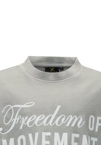 Hellgrauer Pullover mit hohem Kragen. Enthält weißen Text: "Freiheit der Bewegung" in auffälliger Schrift. Weiche, baumwollähnliche Textur.