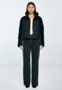 Černá péřová bunda s fleecovými rukávy, vysokým límcem a zipovým zapínáním. Doplněná o tmavé široké džíny pro sladěný vzhled.