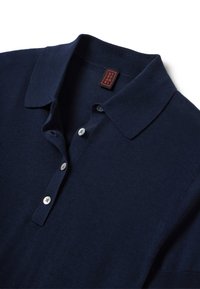 Polo shirt blu navy realizzato in tessuto a maglia, con colletto, patta a tre bottoni e un'etichetta rossa e nera cucita all'interno del collo.