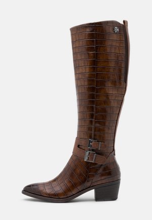 Botte haute en cuir marron motif crocodile, deux boucles latérales, petit talon carré et un petit détail fleur en métal près du haut.