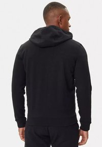 Felpa nera con cappuccio realizzata in un morbido tessuto, dotata di tasca a marsupio e polsini a costine, mostrata da dietro. Design semplice e minimalista.