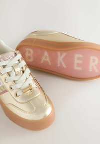 Kuldseid metallist tossusid valgete paelte ja karamellikujuliste talladega, kus ühelt tossult paistab roosa poolläbipaistev tall ning seal on kirjas "BAKER".