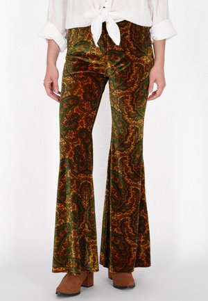 Pantaloni a campana in velluto con motivo paisley marrone e verde, dalla morbida texture, indossati con un top bianco annodato e stivali con tacco a blocco marroni.