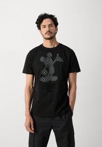 Camiseta de algodón negra con un gráfico de Mickey Mouse en patrón de tablero de ajedrez. Manga corta, cuello redondo y corte relajado.