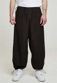 Sorte bredbenede bukser med elastisk talje og snøredetalje, der har en glat overflade og sammensnørede manchetter, parret med hvide sneakers.