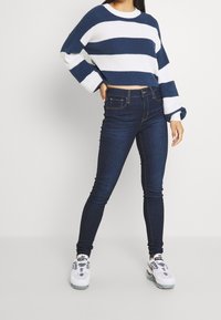 Pull court rayé bleu et blanc à manches longues, assorti à un jean skinny bleu foncé et des baskets blanches avec des accents noirs.