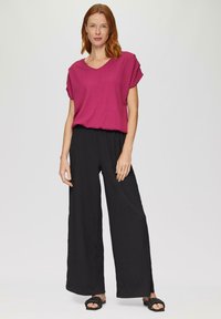 Fuchsia top met korte mouwen en V-hals, gecombineerd met zwarte broek met wijde pijpen in een losse fit en van textuurstof. Zwarte sandalen maken de outfit compleet.