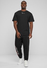 Svart bomull t-skjorte med rund hals og korte ermer, pairt med svarte joggebukser med hvite og røde logo-trykk, og hvite joggesko.