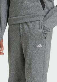 Pantalones deportivos grises con una tela texturizada, con bolsillos laterales y un pequeño logo blanco en la pierna izquierda. Diseño de cinturilla suave y elástica.