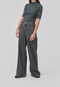 Grijs geribbeld T-shirt met korte mouwen, gecombineerd met hoog-waist brede grijze denim jeans. De jeans hebben een knoopsluiting en voorzakken.