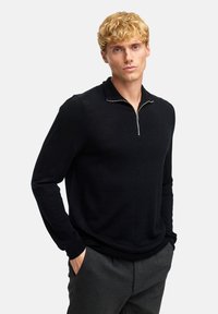 Zwarte, lange mouwen pullover met een ritskraag. Zachte, gebreide textuur. Gecombineerd met grijze broek. Eenvoudig, modern ontwerp.