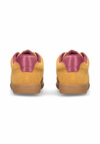 Paire de baskets en daim jaune avec des contreforts de talon en cuir rose et des semelles en caoutchouc gomme vues de dos sur fond blanc.