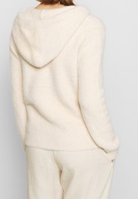 Kremowa, miękka bluza z dzianiny o fakturowanym wykończeniu, z prążkowanymi detalami na dole i mankietach oraz dużym, zaokrąglonym kapturem.