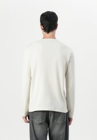 Long-sleeve cream shirt with a round neckline and soft texture, paired with dark gray jeans featuring a classic pocket design.