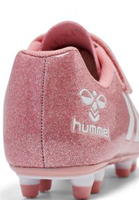 Chaussure de football rose pailletée avec logo "hummel" blanc et crampons blancs et roses sur la semelle extérieure, vue de l'arrière.