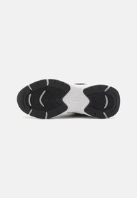 Black and white sneaker sole featuring textured rubber, curved grooves for grip, and a logo imprint in the center.