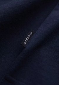 Tmavě modrá bavlněná látka s hladkým povrchem, na které je našita malá černá etiketa se slovem "ombre".