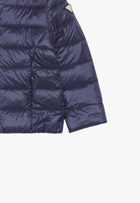 Navy blue puffer jacket with horizontal quilted design. Features a triangular logo and a side zip pocket. Smooth, shiny fabric.