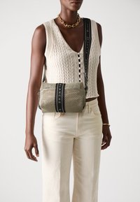 Borsa in maglia beige con dettaglio nero e testo "BLANCHE". Forma rettangolare compatta con chiusura a zip superiore.