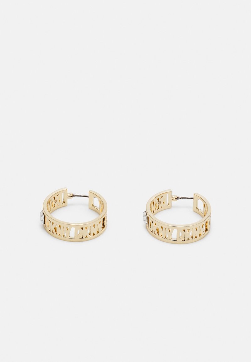Paire de boucles d'oreilles créoles dorées avec logo DKNY découpé et tiges métalliques sur fond blanc.