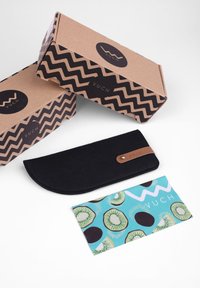 Černé plstěné pouzdro s koženým detailem, umístěné vedle dvou vzorovaných kartonových krabic s cik-cak vzory a tyrkysové karty se vzorem kiwi.