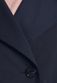 Blazer bleu marin cu un rever lat, cusături curate și un nasture lucios de culoare neagră cu un design cu patru găuri. Strat interior prezintă o textură roz deschis.