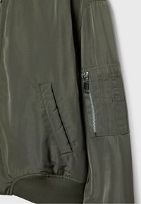 Olijfgroene bomberjack met een gladde stof, geribbelde manchetten, zijzakken en een ritssluiting op de mouw met textuurdetails.
