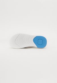 Hvit sneakersåle med blå aksent, med et teksturert gripe-design og uttalte bølgemønstre for bedre grep.