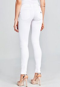 Jeans blancos ajustados con una cinturilla alta, que cuentan con dos bolsillos traseros. Combinados con sandalias de tacón alto en beige con un acento metálico.