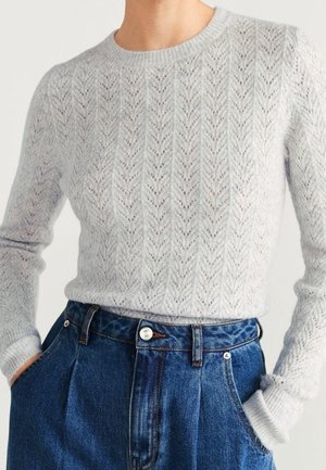 Lichtgrijze gebreide trui met een chevronpatroon, ronde hals en lange mouwen. Gecombineerd met high-waisted denim jeans.