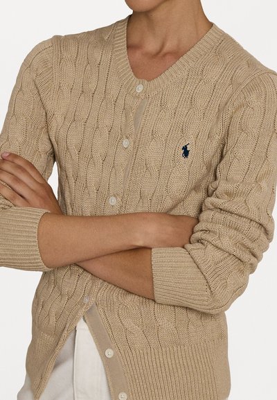 Cardigan en tricot beige avec un motif en cable, col en V et fermeture à boutons. Comprend des poignets côtelés et un petit logo brodé.