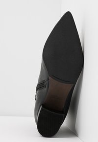 Bottine noire en cuir à bout pointu vue de la semelle, avec une semelle texturée au talon et à l’avant, avec une fermeture éclair latérale.