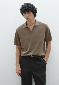 Polo shirt marrone a maniche corte con colletto a scollo a V, abbinato a pantaloni neri e una cintura intrecciata. Tessuto semplice con texture liscia.
