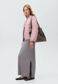 Giacca trapuntata rosa, abito maxi grigio a coste con spacco laterale, ballerine nere. Modella porta una borsa grigia scura con borchie. Sfondo minimale.