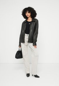 Crna kožna jakna, pripijena crna košulja, svijetlosive traperice širokih nogavica i crna torbica. Model nosi elegantne crne šiljate štikle.